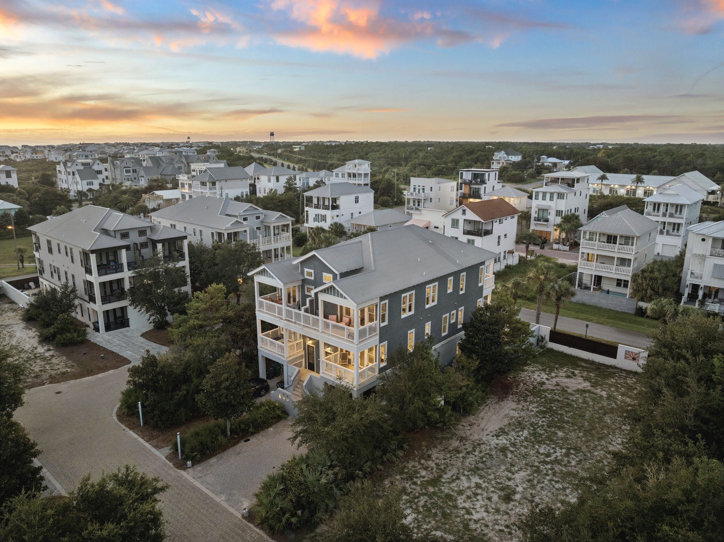 This elegant coastal home sits nestled among palm-lined streets in a serene beachside neighborhood. The warm glow of sunset illuminates its classic architecture, surrounded by lush greenery and just moments from the shore.