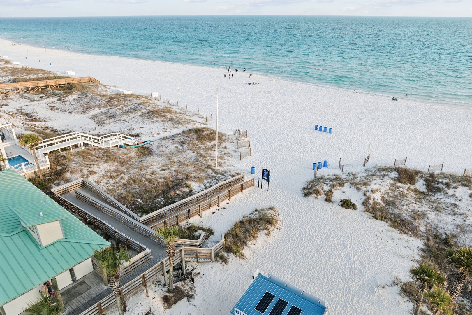 Pristine white sand beach stretches along crystal-clear turquoise waters with beach access walkways and coastal facilities nearby.