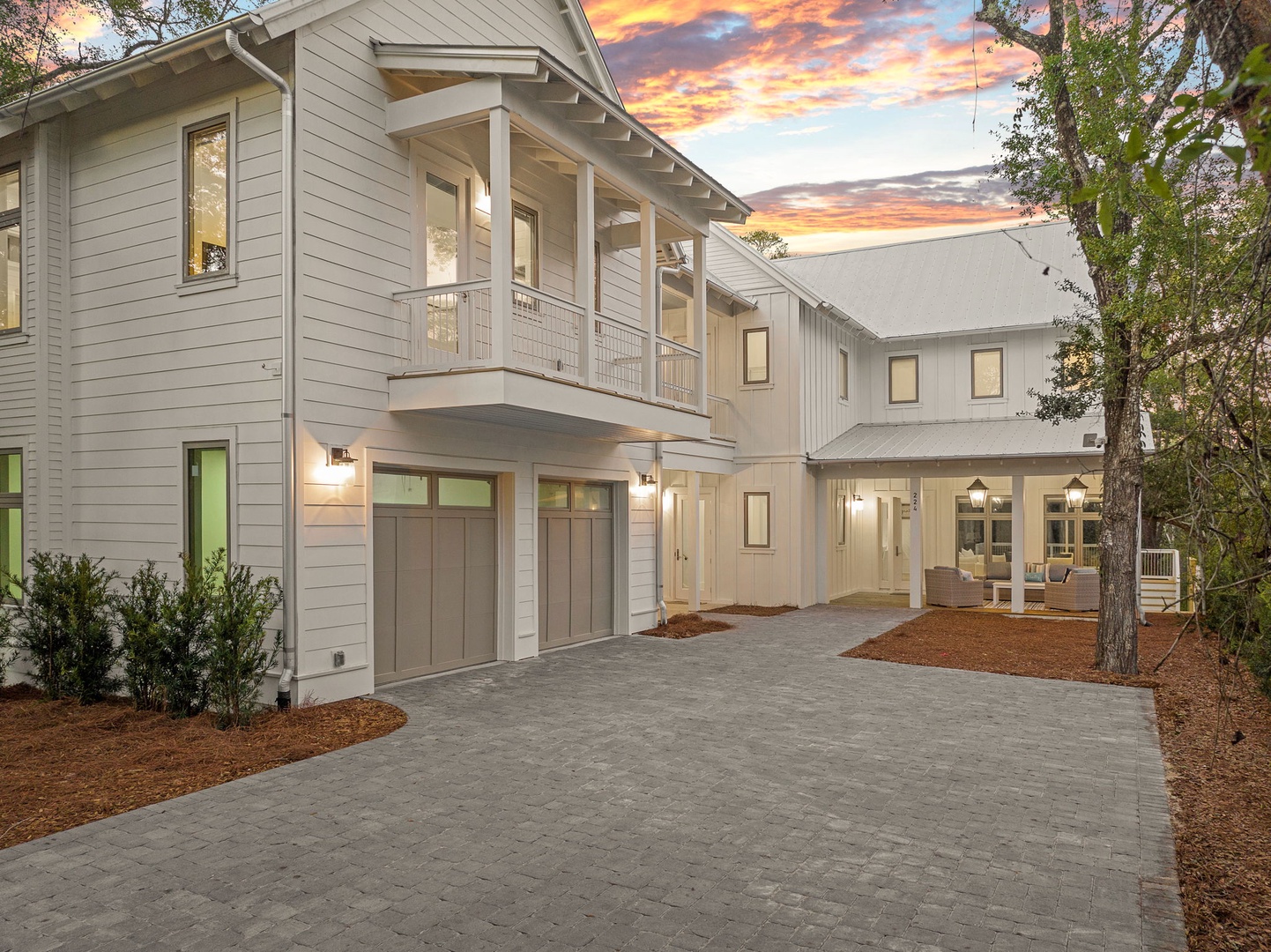 Contemporary coastal architecture framed by mature trees and a dramatic sunset sky creates an impressive arrival experience.