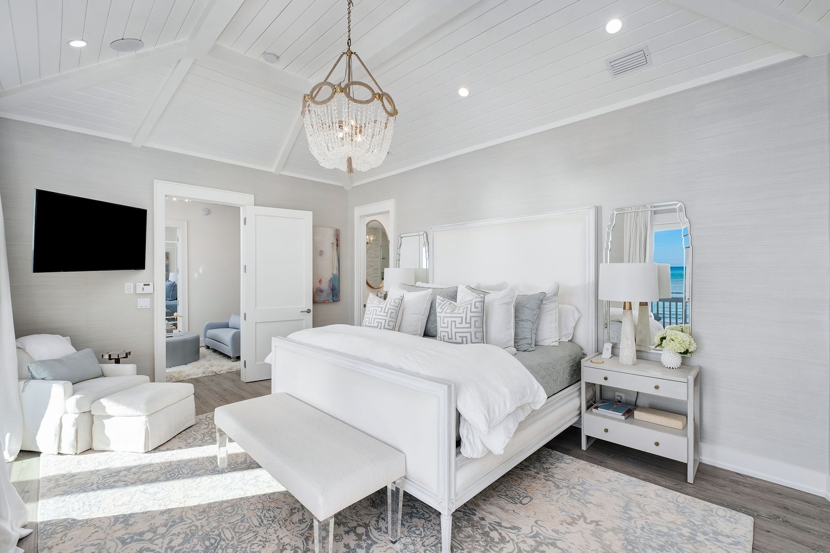 Unwind in your elegant bedroom retreat with vaulted ceilings, plush bedding, and a stunning ocean view framed by airy windows—your perfect coastal escape awaits.
