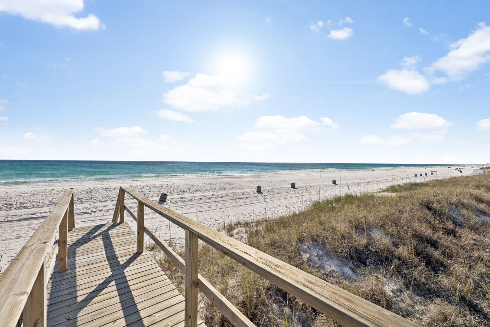 Pristine white sand beach with turquoise waters stretches endlessly along the coast, accessed by wooden boardwalk through natural dunes.