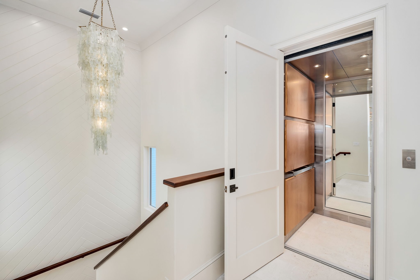 Elegant elevator access awaits you, framed by a stunning chandelier and pristine white shiplap walls that create a sophisticated arrival experience.