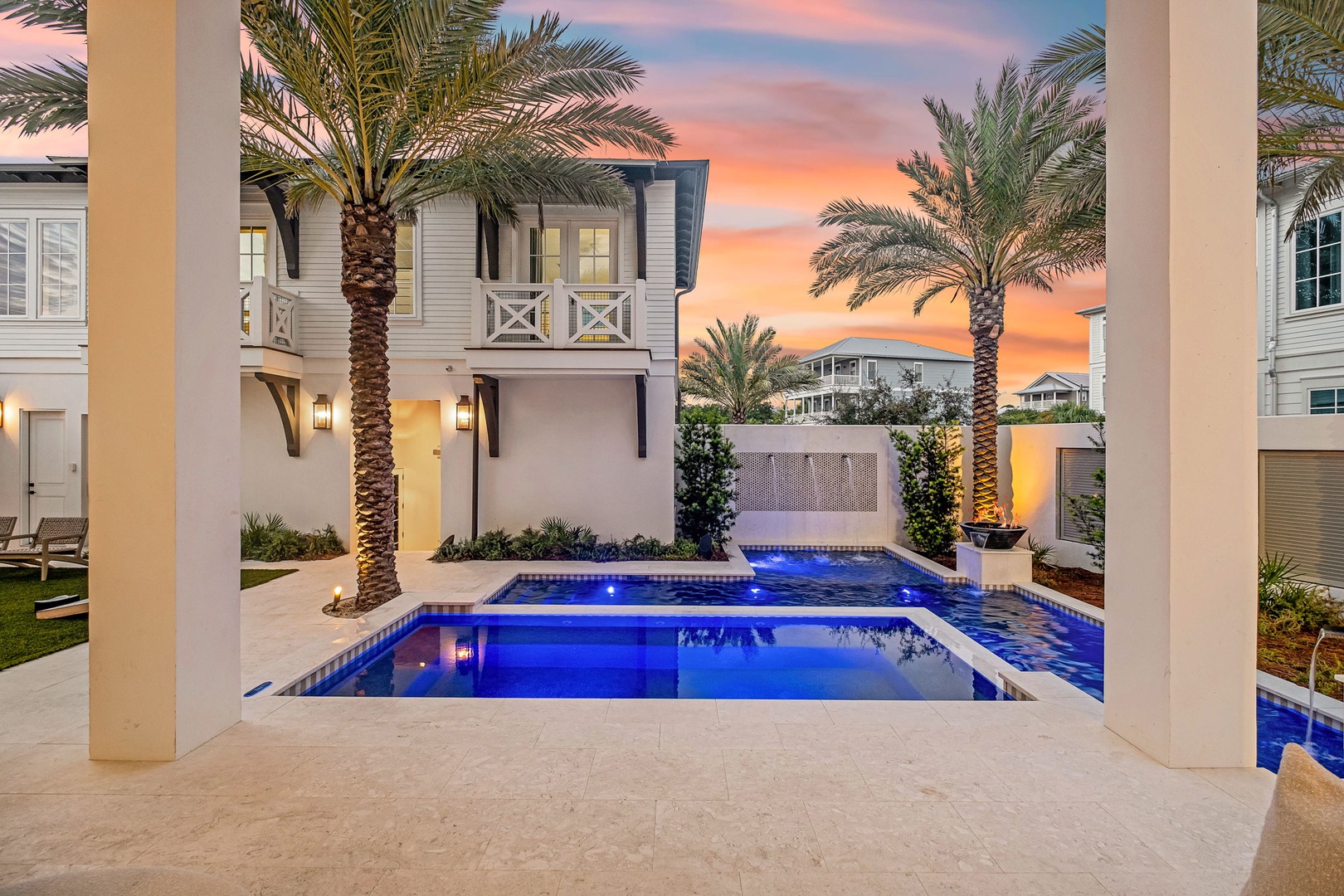 A stunning evening view of the property's pool area framed by towering palms and vibrant sunset hues, creating an inviting backdrop for your coastal retreat.
