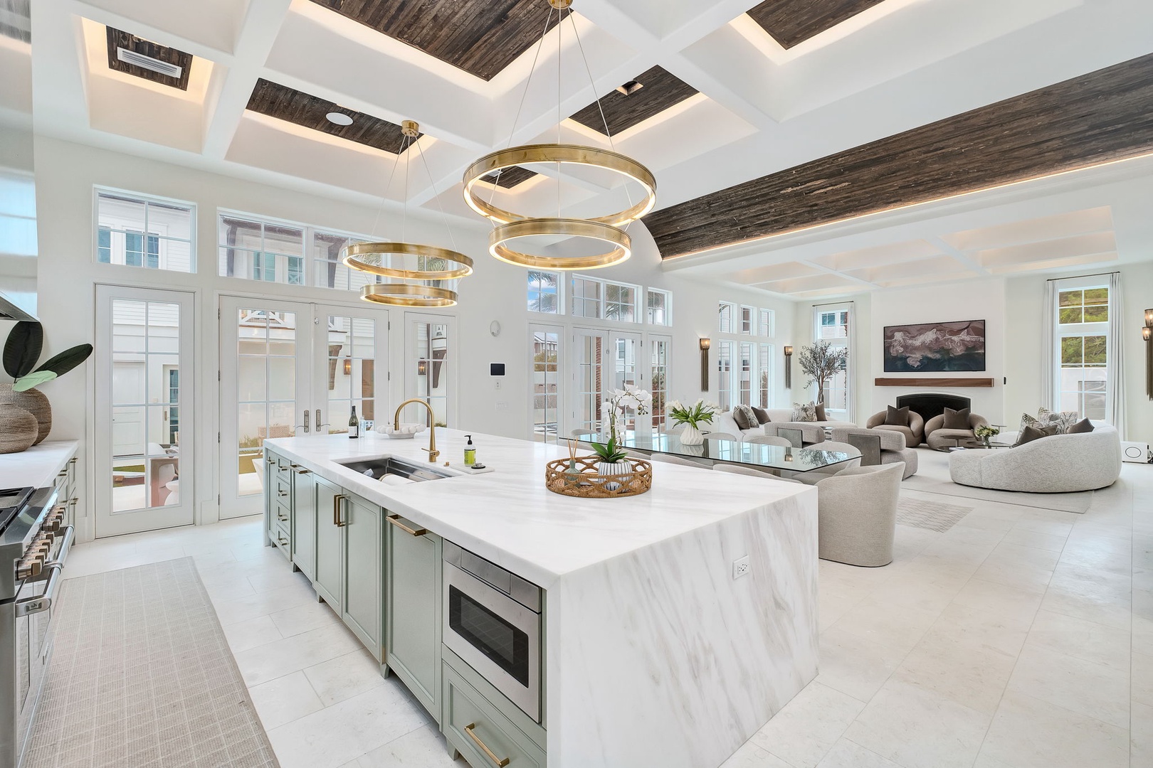 Sunlight streams through soaring ceilings into your chef's kitchen and living space. The marble waterfall island invites you to gather while golden chandeliers add warmth overhead.