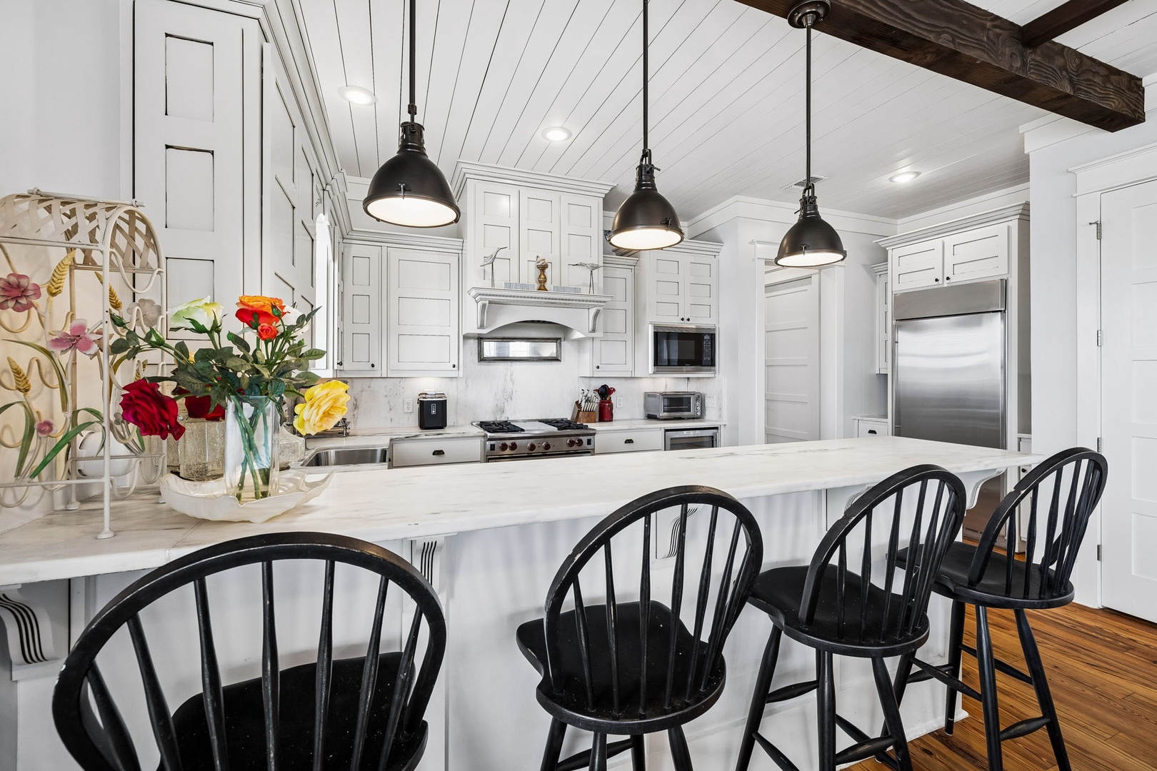 Step into your gourmet kitchen where rustic wooden beams meet elegant white cabinetry. The spacious marble island invites you to gather with friends, while fresh flowers add a welcoming touch to your home away from home.