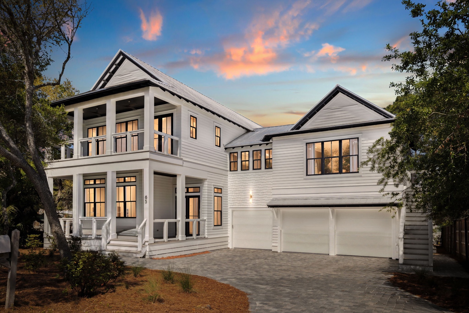Modern coastal home with warm evening lighting and dramatic sunset sky creates a welcoming arrival experience.