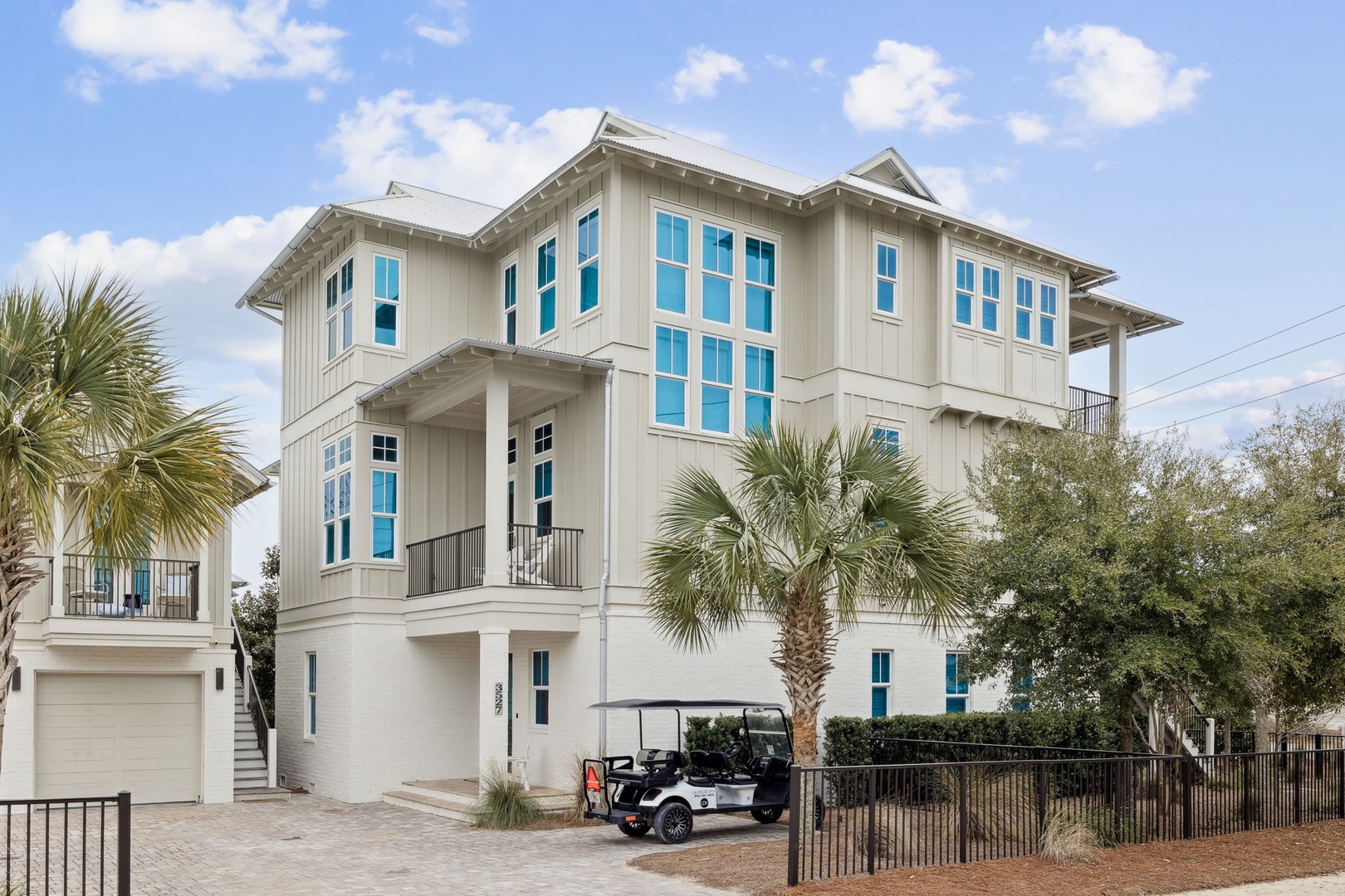 Modern three-story beach house with coastal charm, surrounded by palm trees and tropical landscaping in a peaceful neighborhood setting.