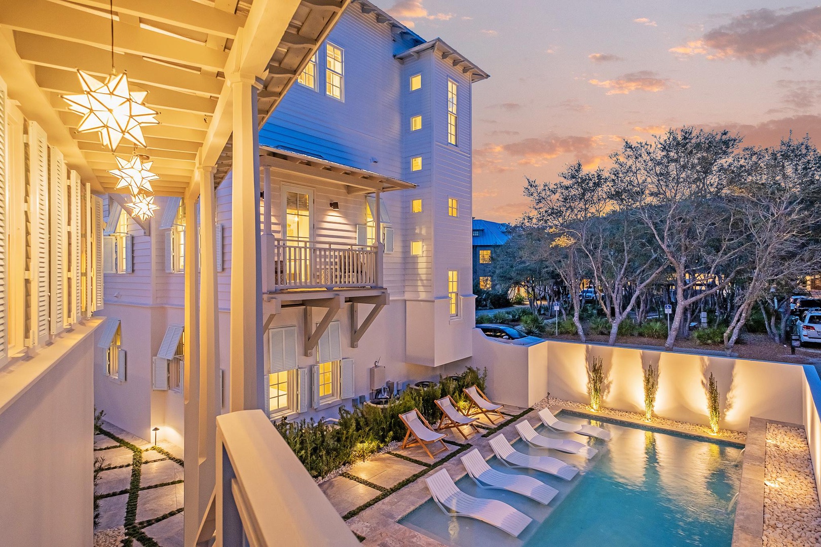 A stunning multi-story property featuring a private pool and elegant outdoor space, illuminated by warm evening light in a beautifully landscaped neighborhood setting.