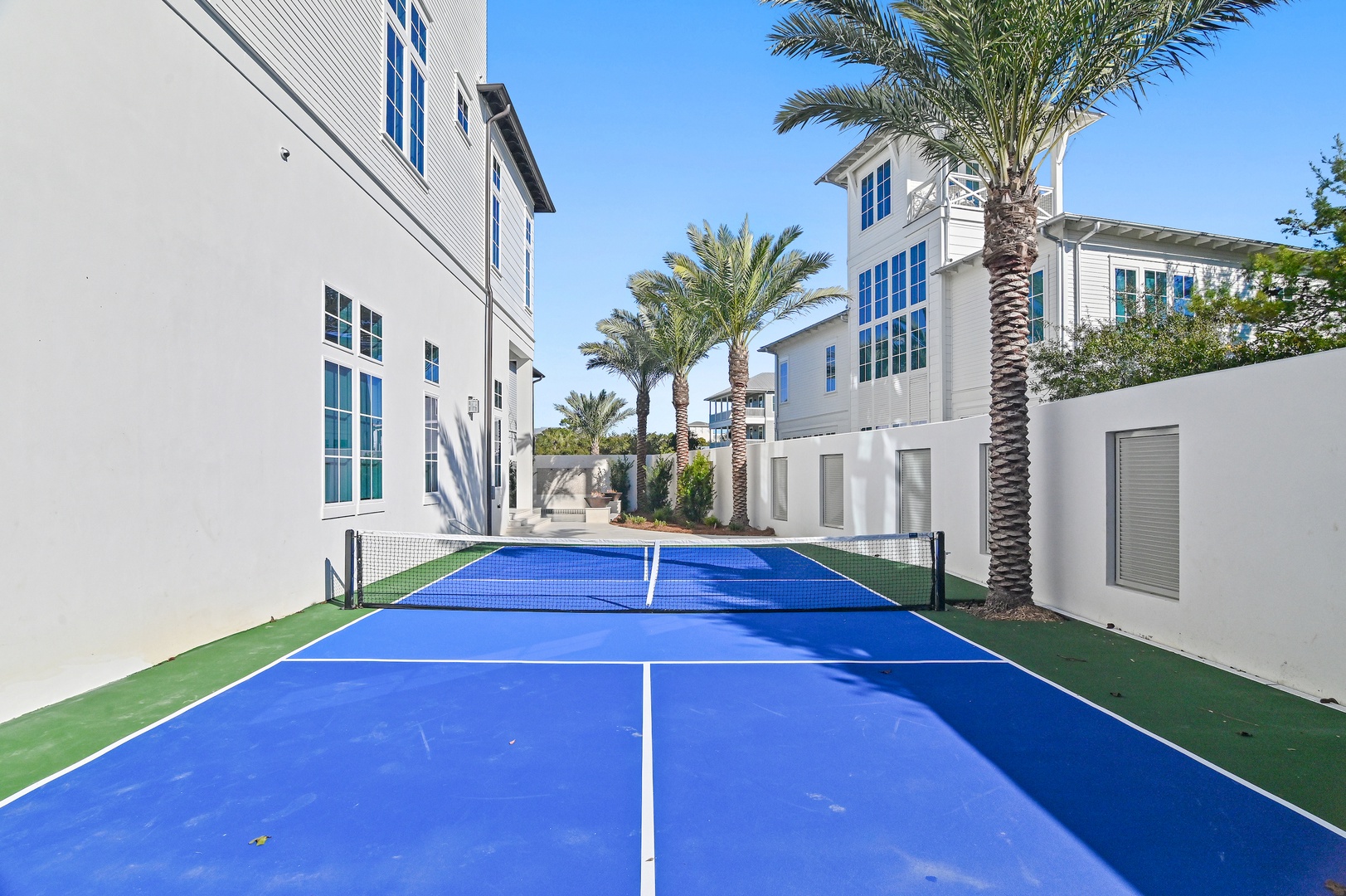 Private tennis court nestled among palm trees and modern architecture, offering guests an exclusive space for matches and active recreation under sunny skies.