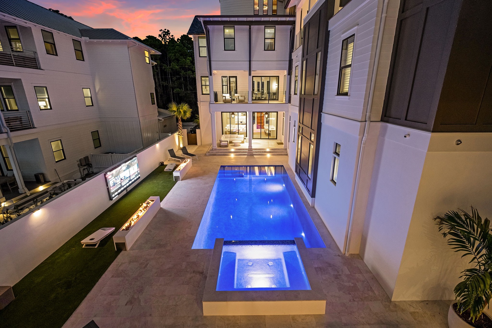 This stunning property features a private pool and spa illuminated beneath a breathtaking sunset sky, surrounded by elegant outdoor living spaces and a well-appointed multi-level home in a coastal community.
