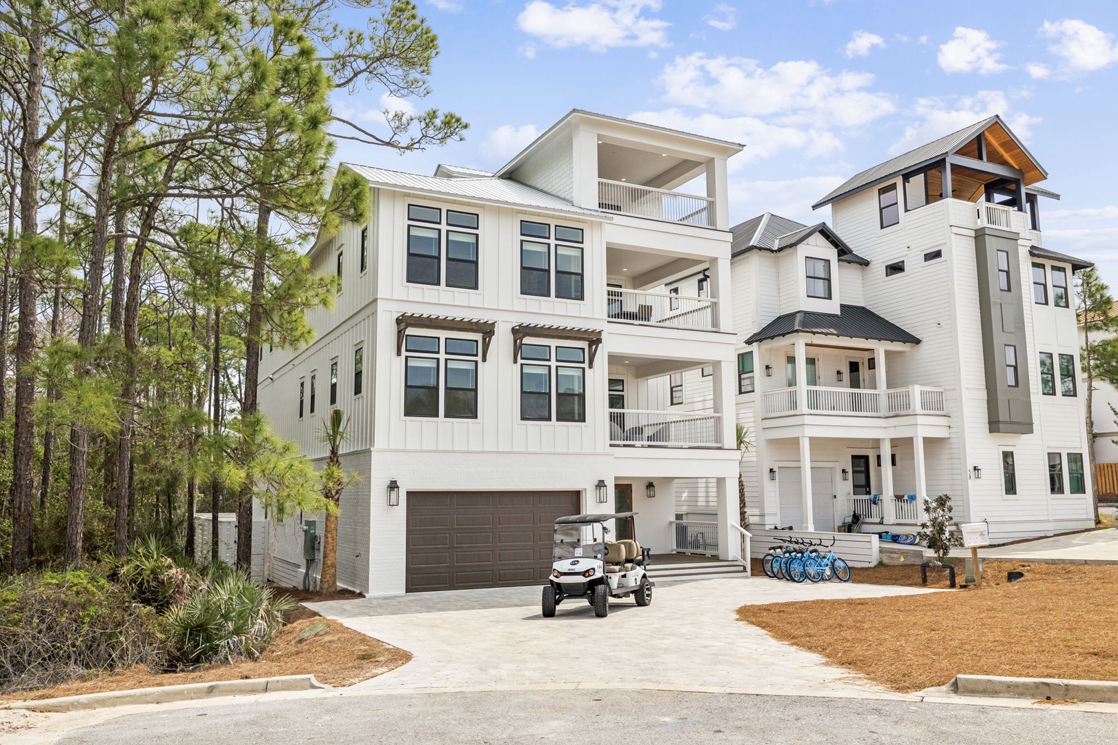 Modern beach house with multiple balconies nestled among towering pines in a peaceful coastal neighborhood.