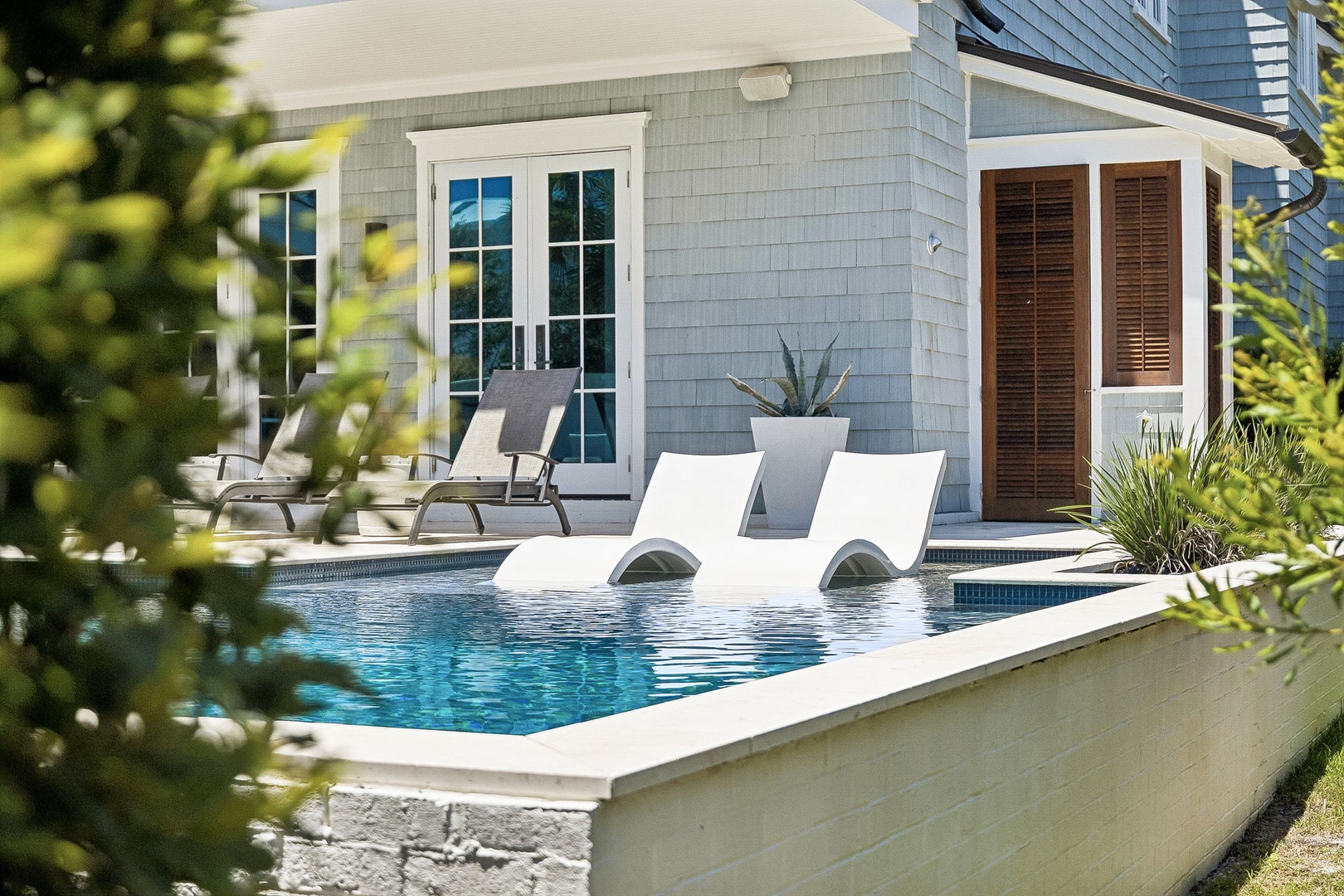 A charming coastal-style property with a private pool, framed by lush greenery and elegant architecture. The inviting aqua waters and poolside loungers create a serene, sun-soaked retreat perfect for relaxation.