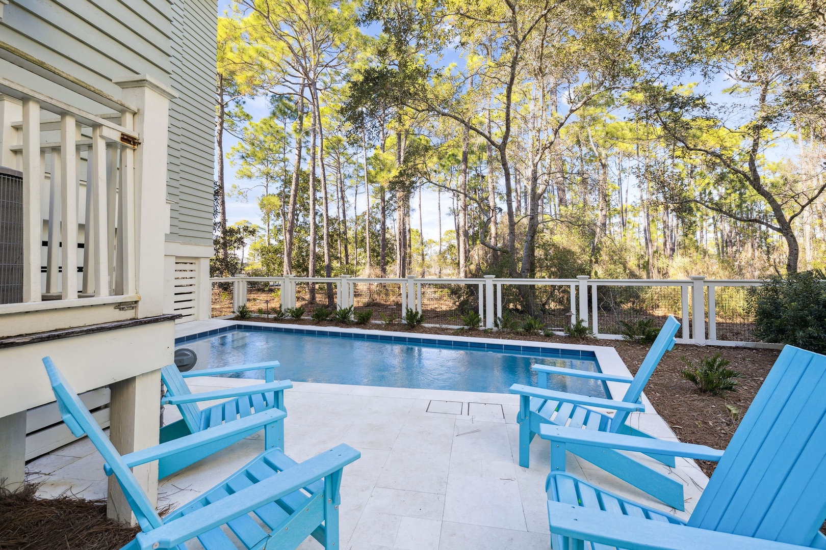 Lounge poolside in cheerful blue chairs, surrounded by towering trees that create your own private forest retreat.
