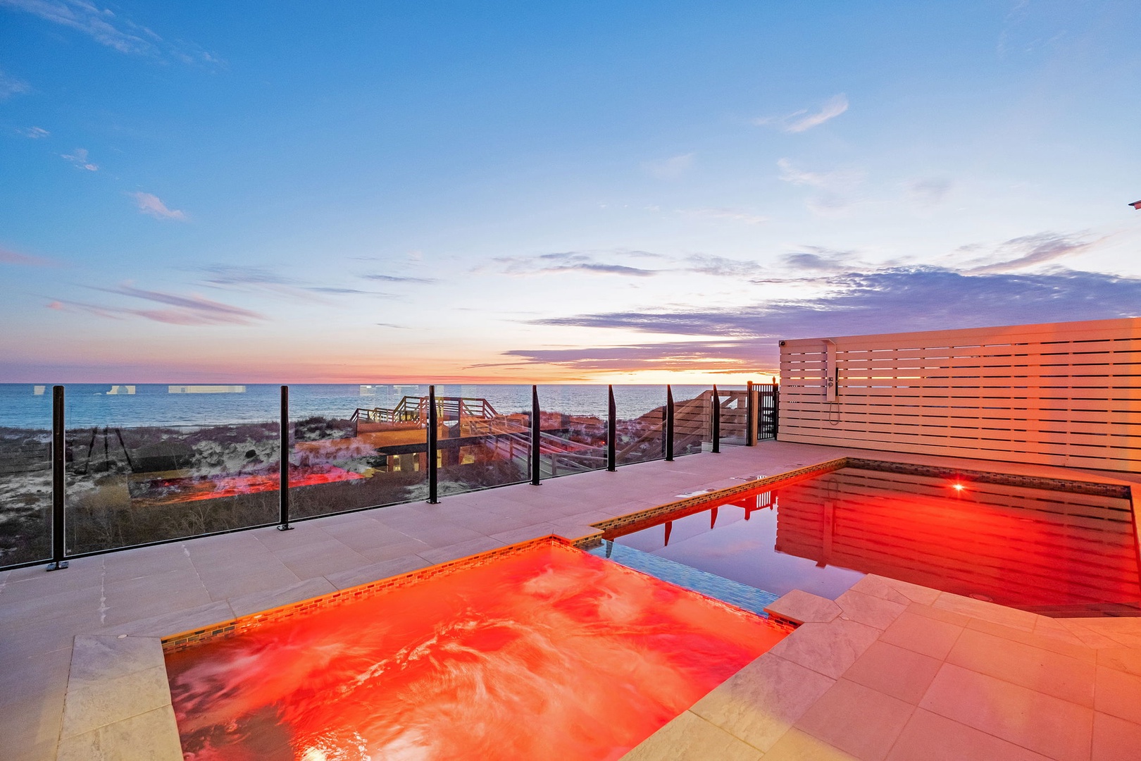 Modern oceanfront terrace with pool overlooking pristine beach during golden hour sunset.