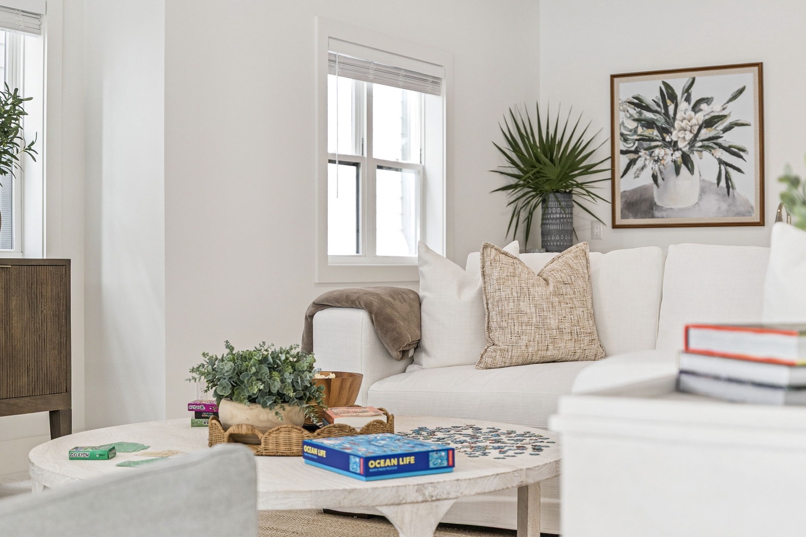 Sink into this bright living space where natural light pours through windows, botanical art adorns crisp white walls, and your favorite book awaits on the marble coffee table.
