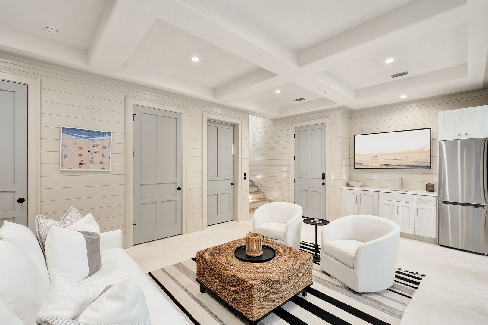 Unwind in your bright living space featuring plush white seating, coffered ceilings, and a fully equipped kitchen ready for your coastal getaway.