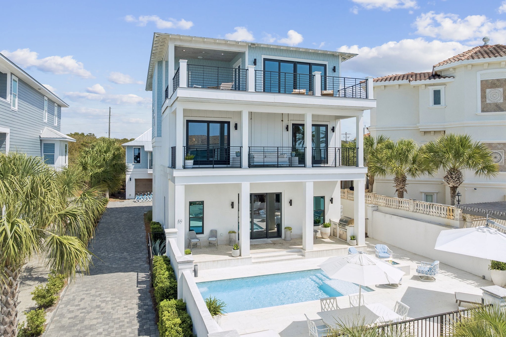 Modern three-story beachside retreat with private pool and tropical landscaping in an upscale coastal neighborhood.