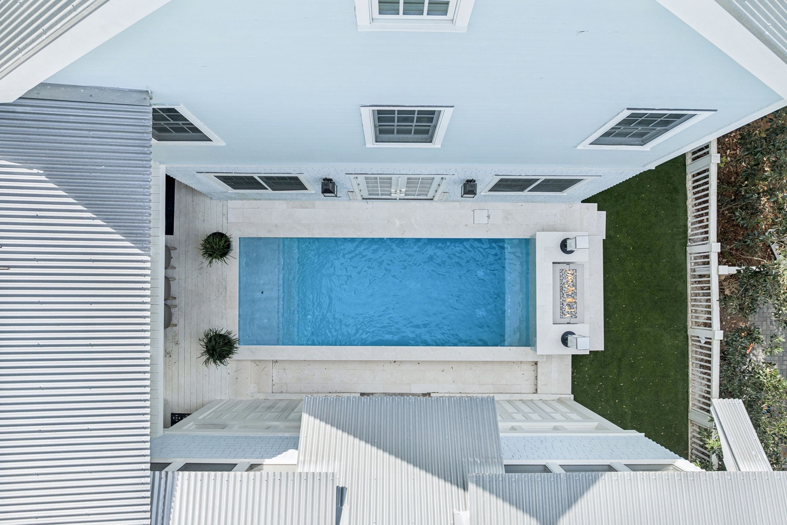 Aerial view of modern property featuring private pool surrounded by white decking and green lawn area.