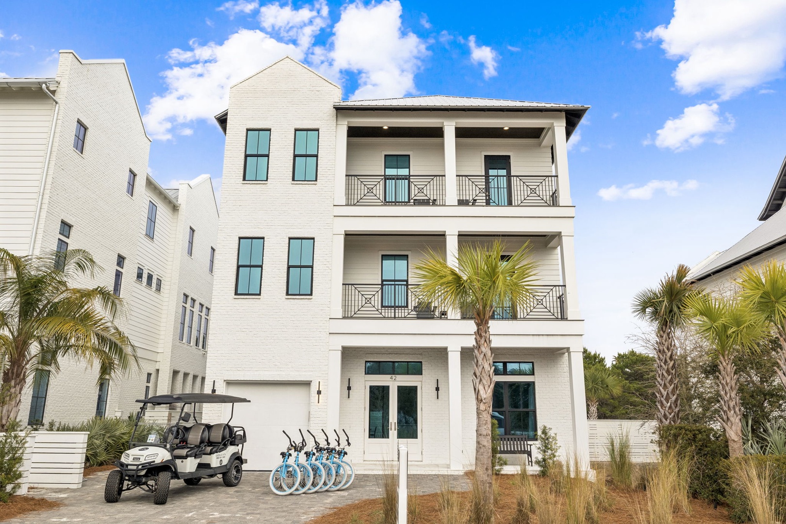 Modern three-story coastal home with palm trees and golf cart, perfect for a beachside getaway in this charming neighborhood.