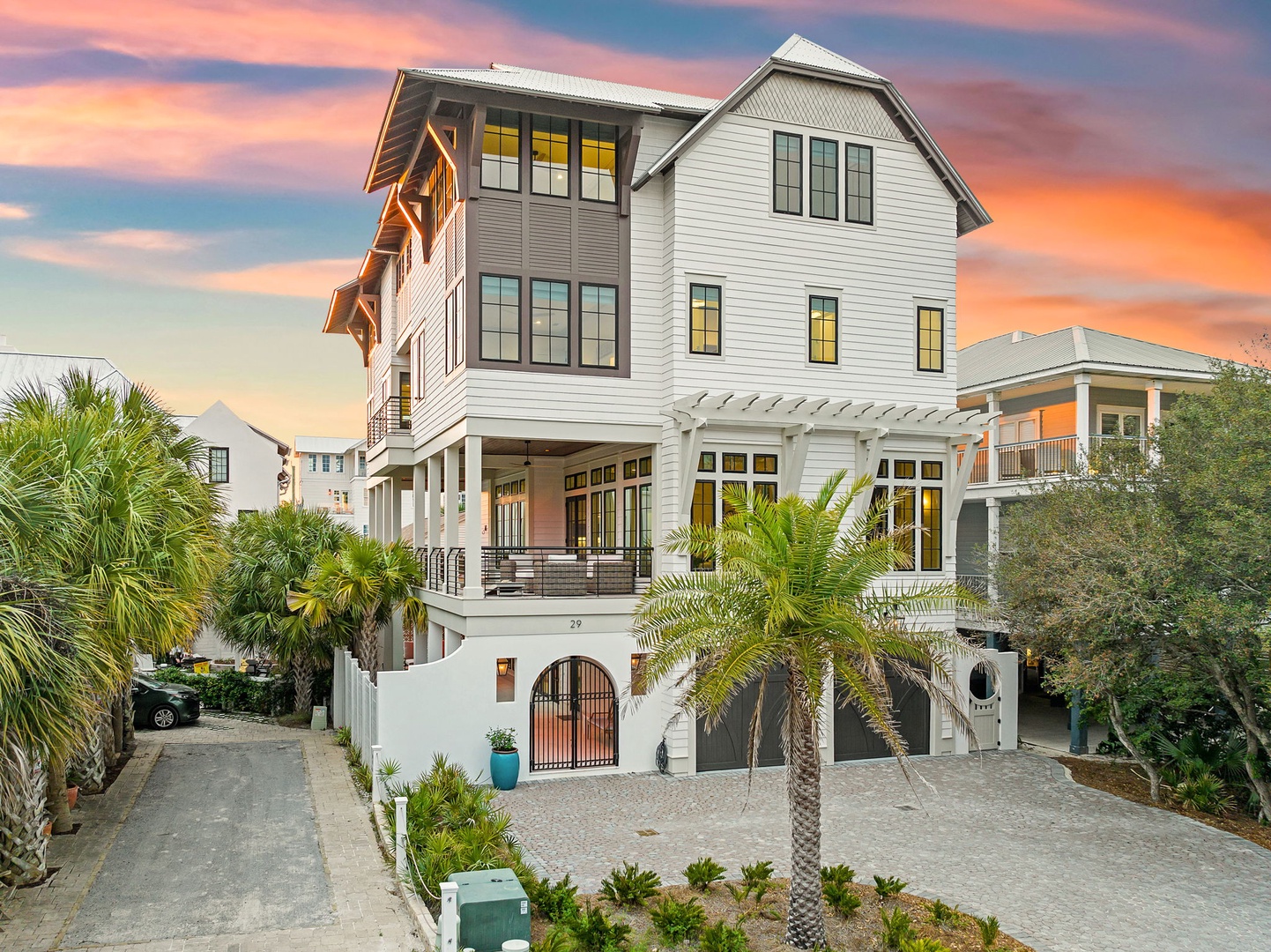 Stunning coastal home with elegant white siding and tropical landscaping showcased against a breathtaking sunset sky.
