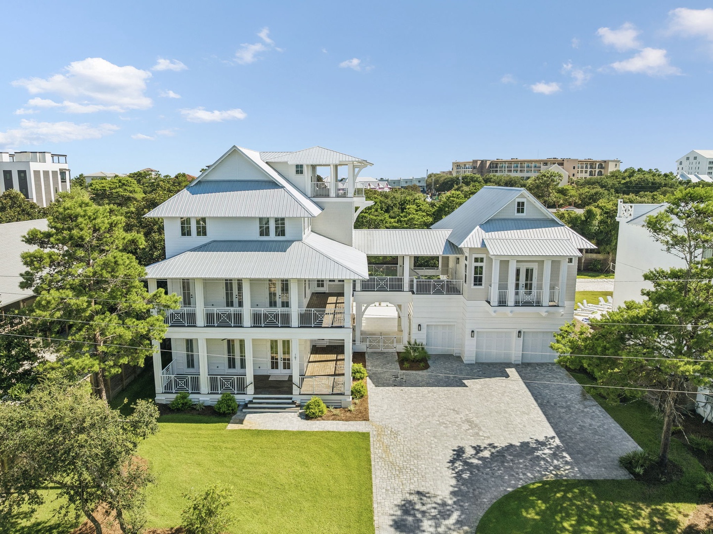 A striking coastal property featuring white metal roofing, multiple balconies, and classic architectural details, nestled among lush greenery in a tranquil residential neighborhood.