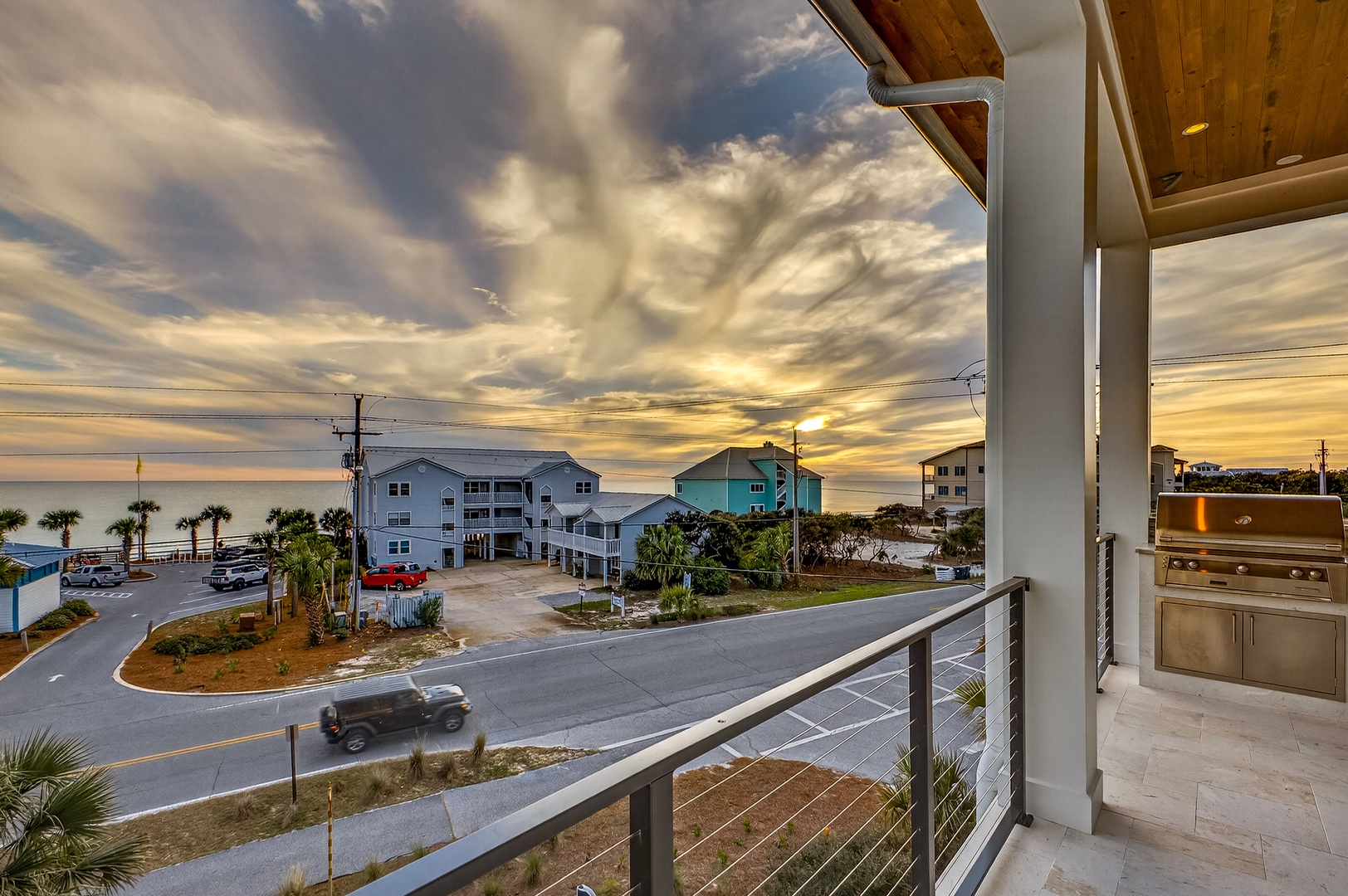 A coastal balcony view showcasing nearby beach houses and palm trees under a dramatic cloudy sky at golden hour.