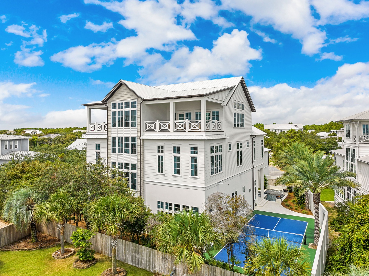 An elegant three-story coastal home with spacious balconies, surrounded by lush palms and a private recreation area—a stylish retreat with abundant natural light and charming architectural details.