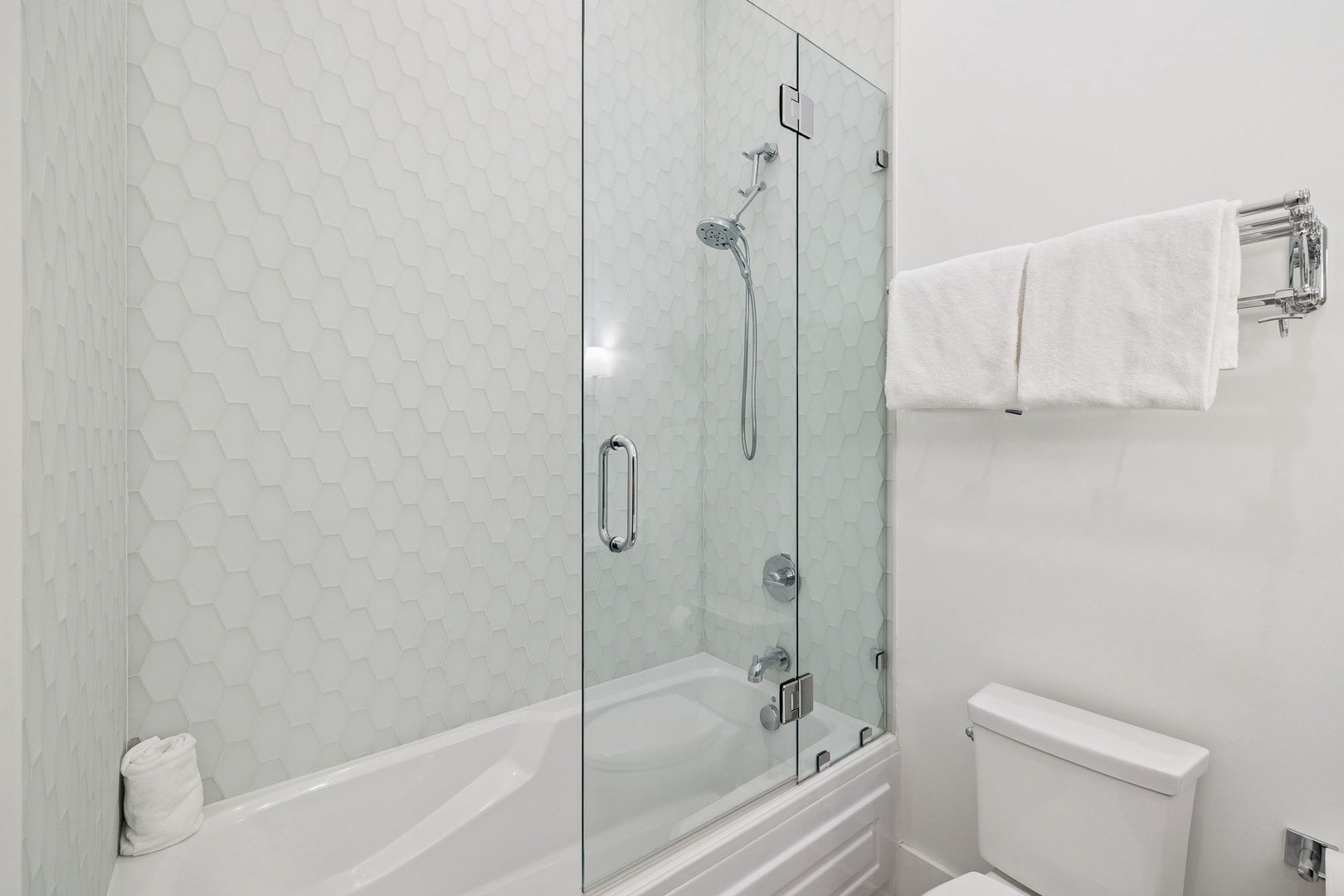 Step into your pristine bathroom where elegant white hexagon tiles and a sleek glass-enclosed tub-shower await your daily refresh.