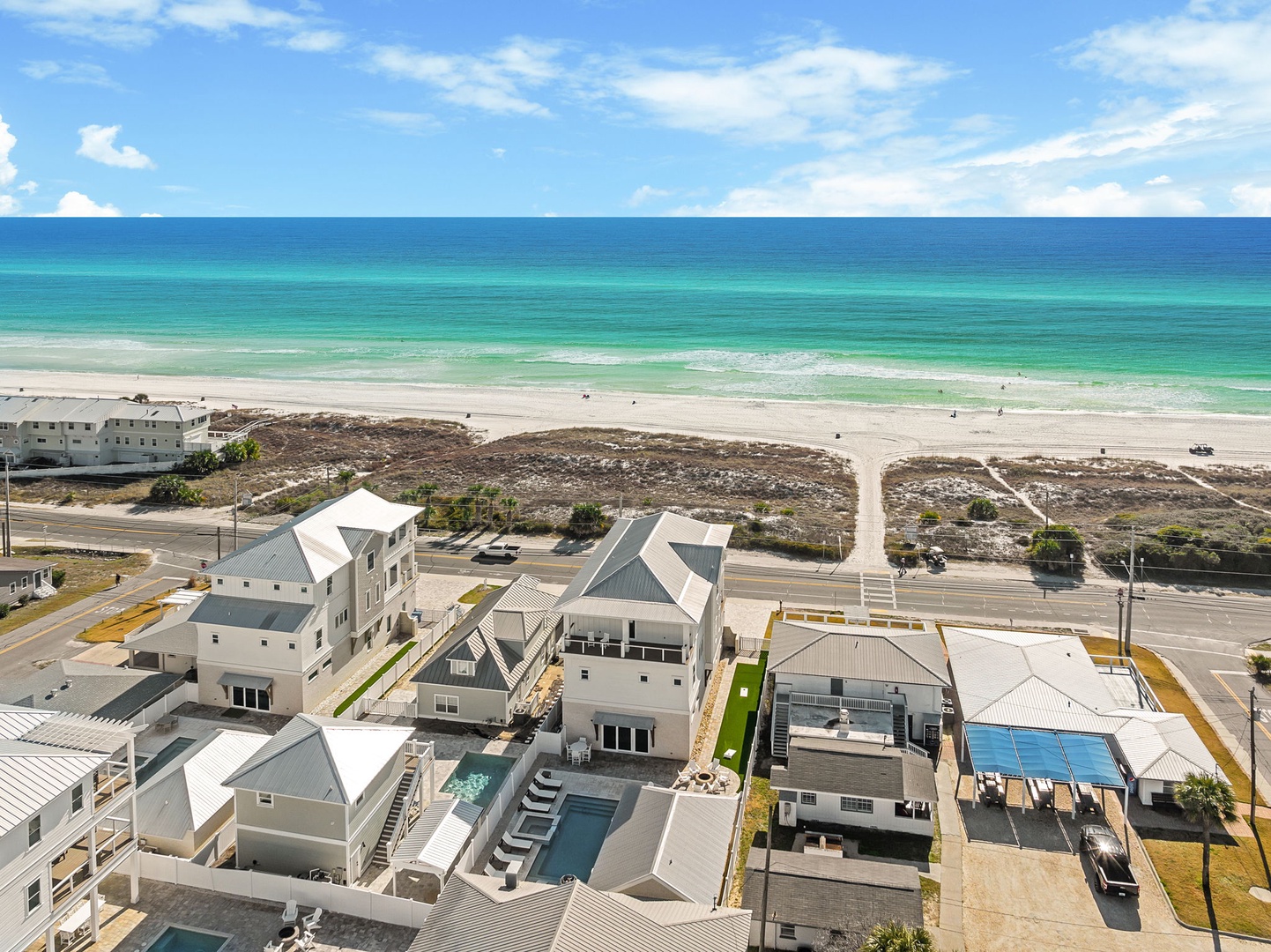 Beachfront vacation rental community with pristine emerald waters and white sandy beach just steps away from modern coastal homes.