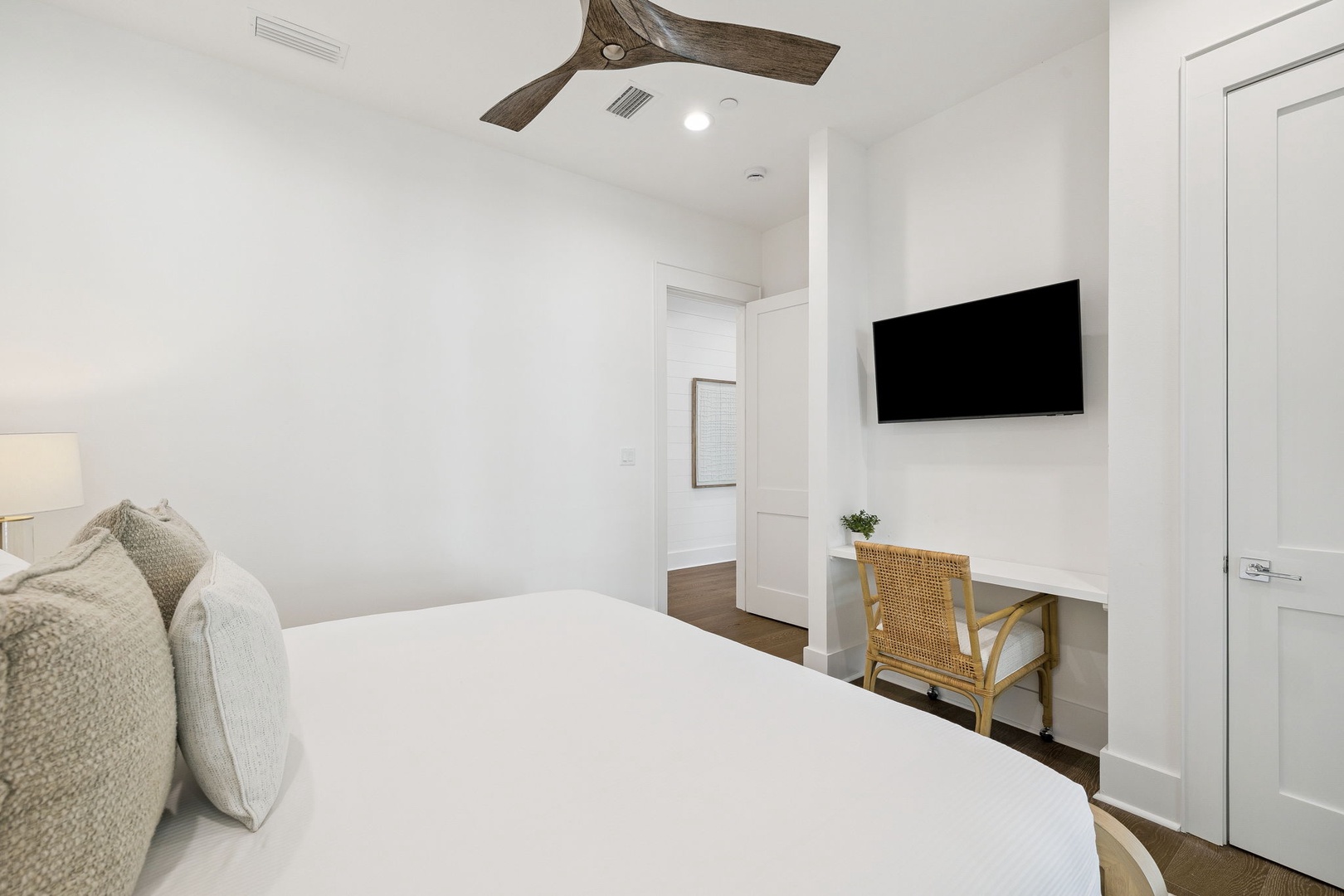 Unwind in your bright, minimalist bedroom with crisp linens, a wall-mounted TV for entertainment, and charming rustic ceiling fan overhead.