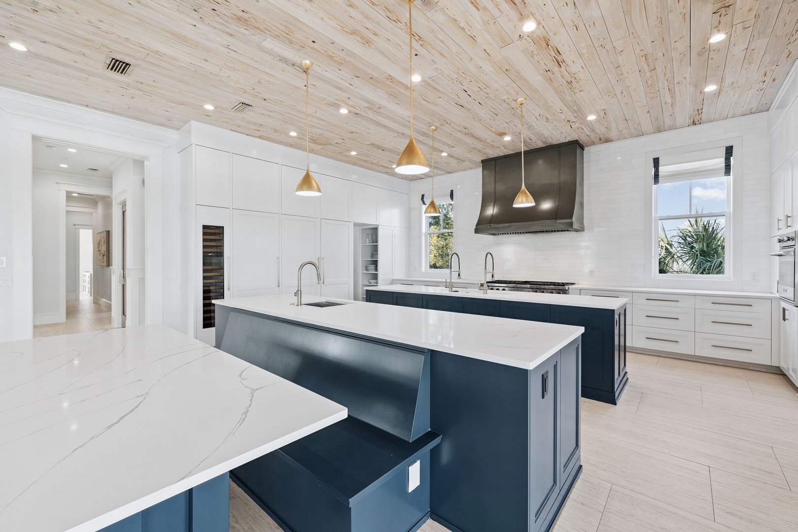 You'll love preparing meals in this stunning gourmet kitchen featuring sleek navy islands, pristine white cabinetry, and warm wood ceilings.