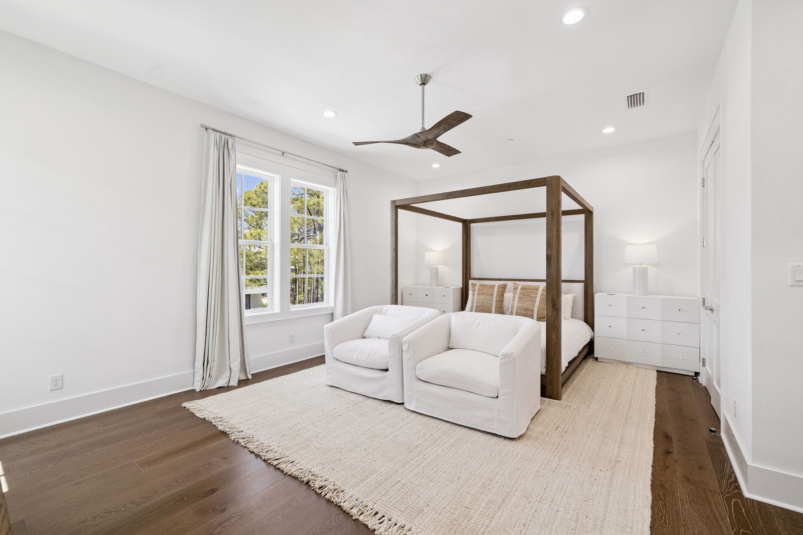 Your stylish master suite features a statement canopy bed, cozy seating area, and serene garden views from large windows.