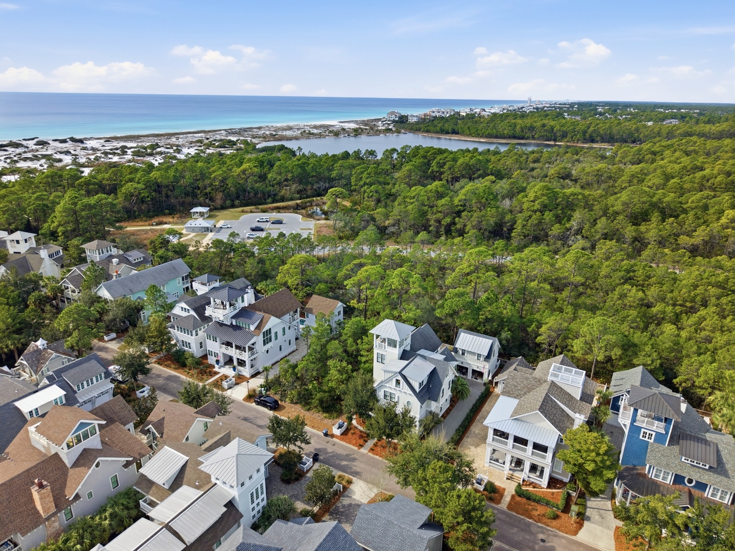 Aerial view showcasing a coastal neighborhood surrounded by lush pine forests, with beach access and serene lakes defining this scenic area.