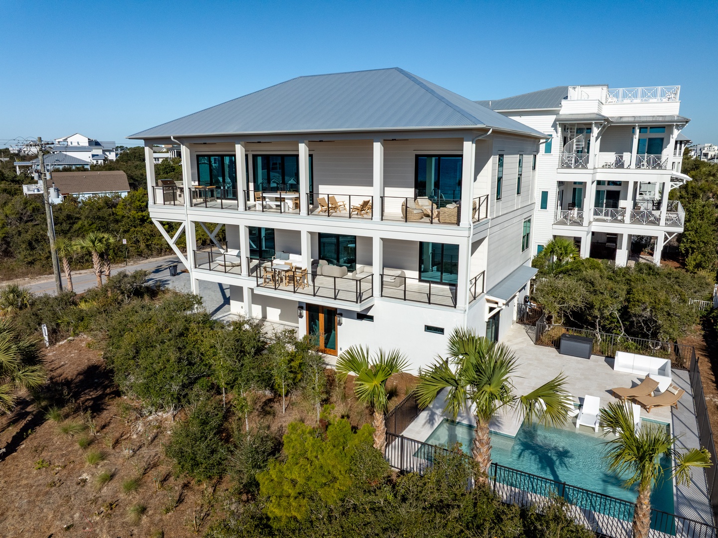 Modern three-story beach house with swimming pool, multiple balconies, and tropical landscaping in a residential coastal neighborhood.