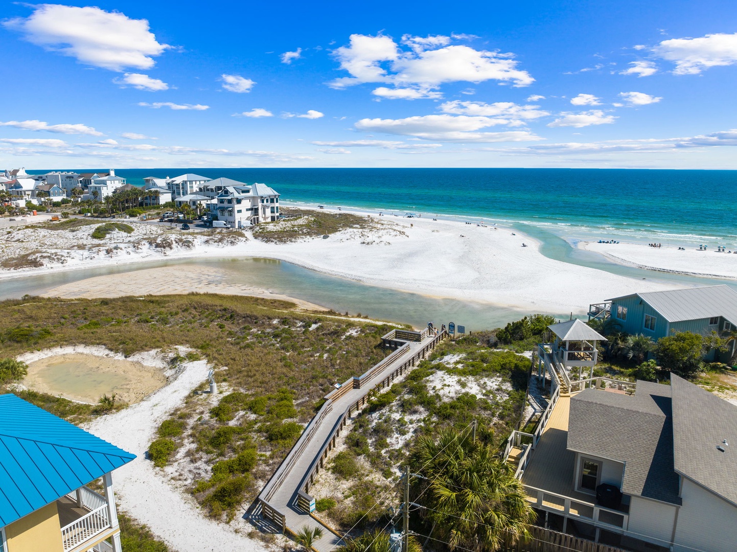 Stunning aerial view of pristine beachfront with crystal-clear waters, white sand dunes, and nearby coastal homes perfect for a seaside getaway.