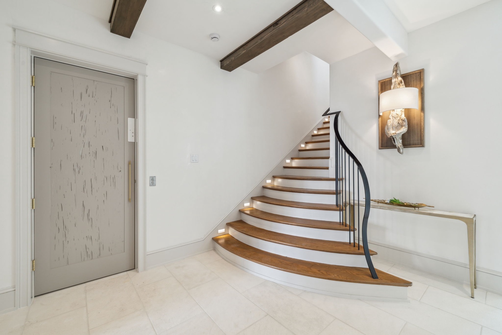 Step through the rustic barn door into your welcoming entryway, where warm wood beams frame soaring ceilings and a gracefully curved staircase beckons you upward toward restful retreat.