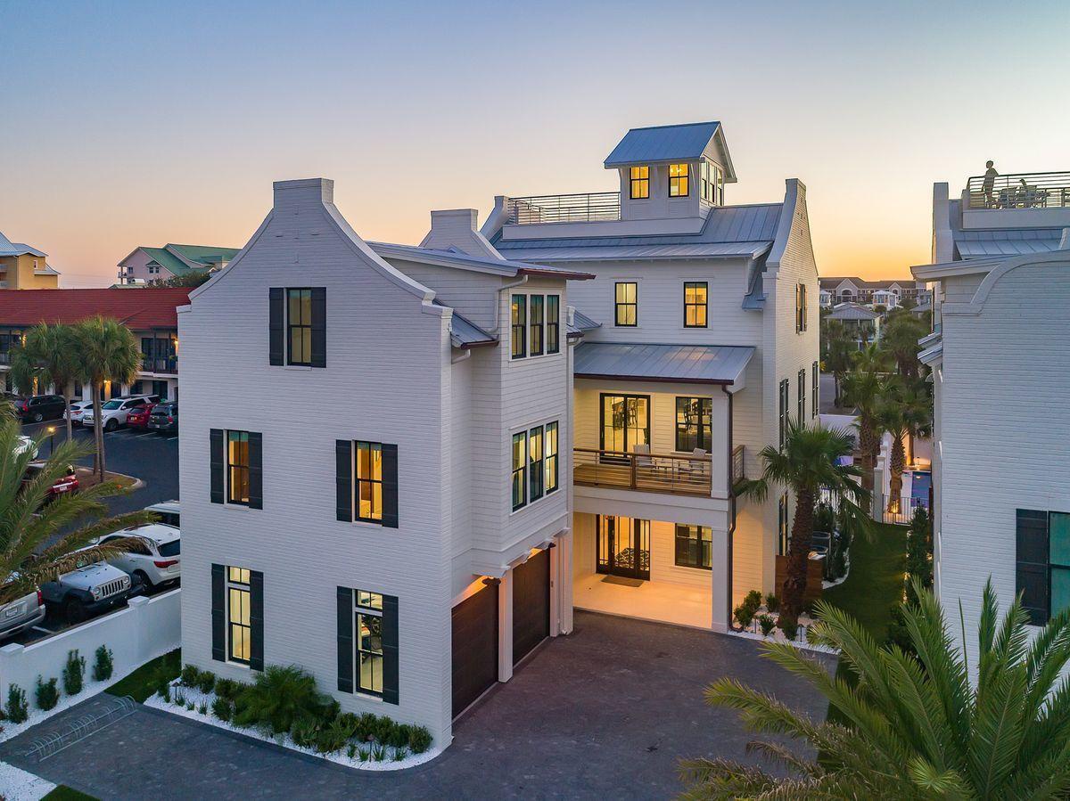 Stunning three-story coastal home with elegant white facade, spacious balconies, and charming rooftop cupola in peaceful residential neighborhood.