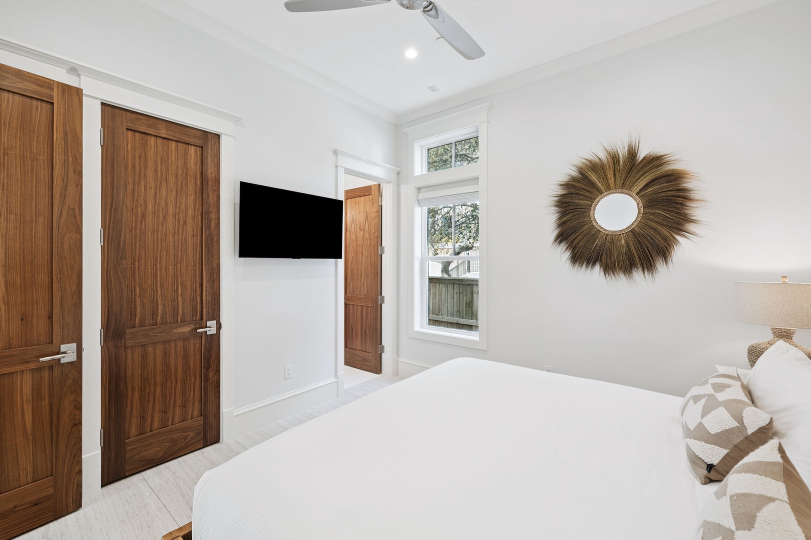 Unwind in your serene bedroom featuring crisp white linens, entertainment system, and natural light streaming through bright windows.