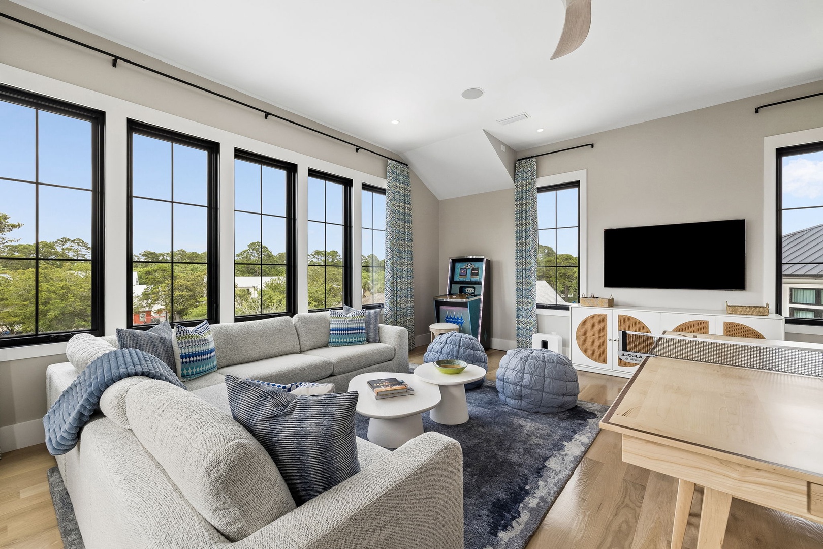 Your living space features plush seating and modern touches, with sunlight streaming through tall windows that frame peaceful greenery beyond.
