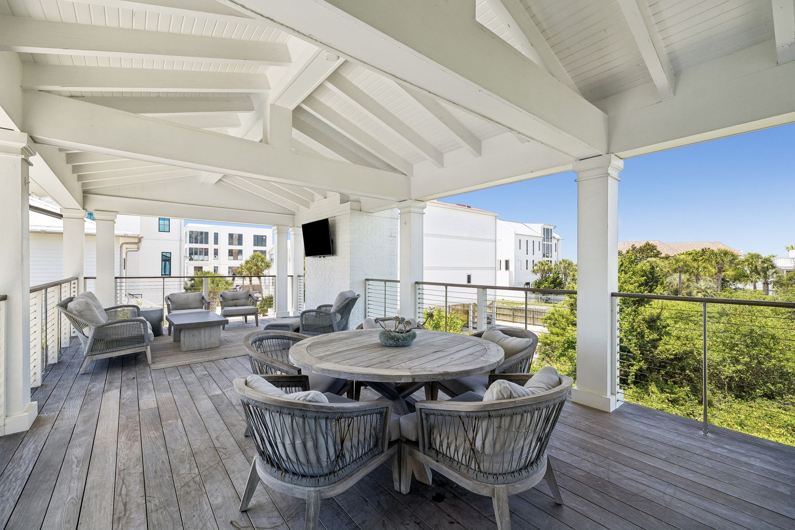 A stunning covered terrace features elegant outdoor furniture and scenic views of lush greenery and neighboring properties, perfect for coastal living and entertaining.