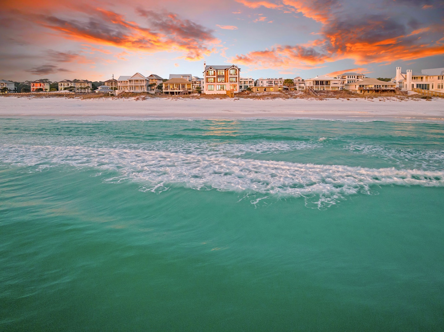 Stunning beachfront properties line pristine white sand beneath a spectacular sunset sky, offering an idyllic coastal retreat setting.