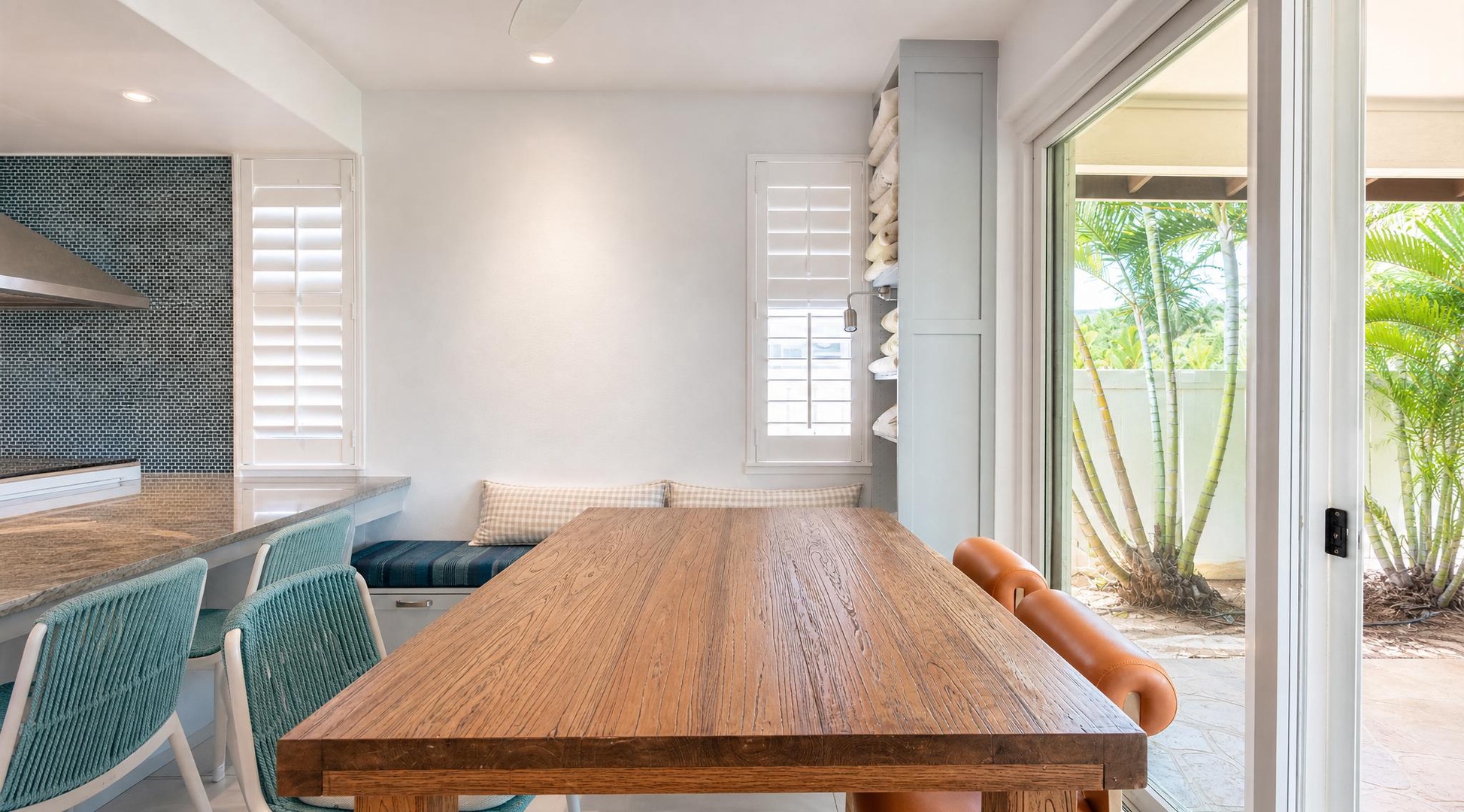 Long wood table by an open sliding door, palms just outside, set for a dinner that runs late.