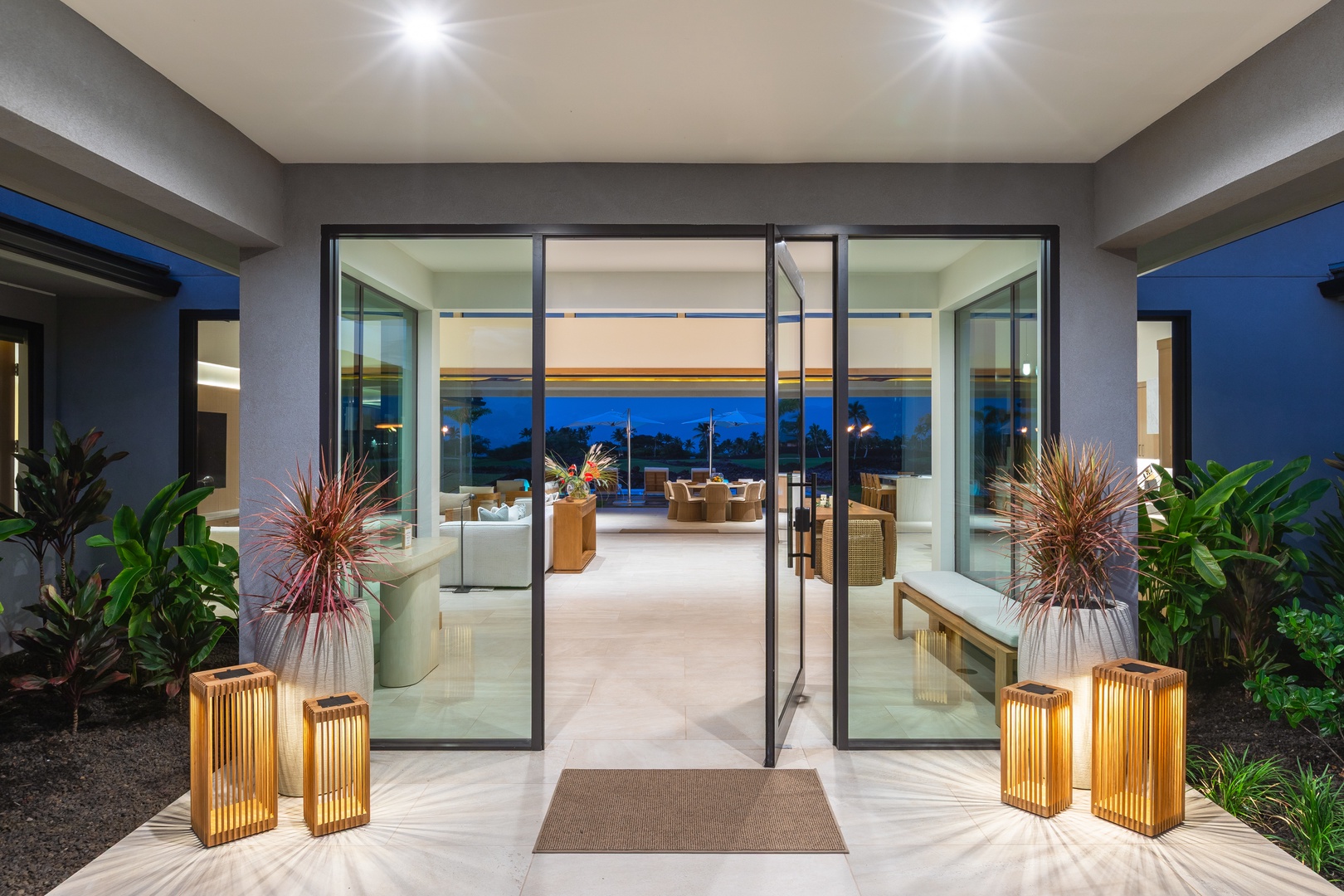 Kamuela Vacation Rentals, 5BD Mauna Lani Lux Ocean Estate (OE12) at One Ocean - Step through elegant glass doors into your luxurious retreat, where warm lighting and tropical plants create an inviting welcome.