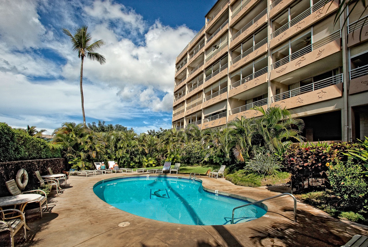 Kihei Vacation Rentals, Kamaole Beach Royal 610 - Palms tower over the pool deck, garden plantings softening the building's edge.