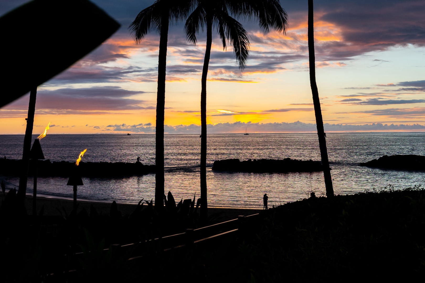 Kapolei Vacation Rentals, Ko Olina Beach Villas B604 - Tropical sunset paints the sky in vibrant hues over calm waters, with silhouetted palm trees framing this breathtaking beachfront scene.