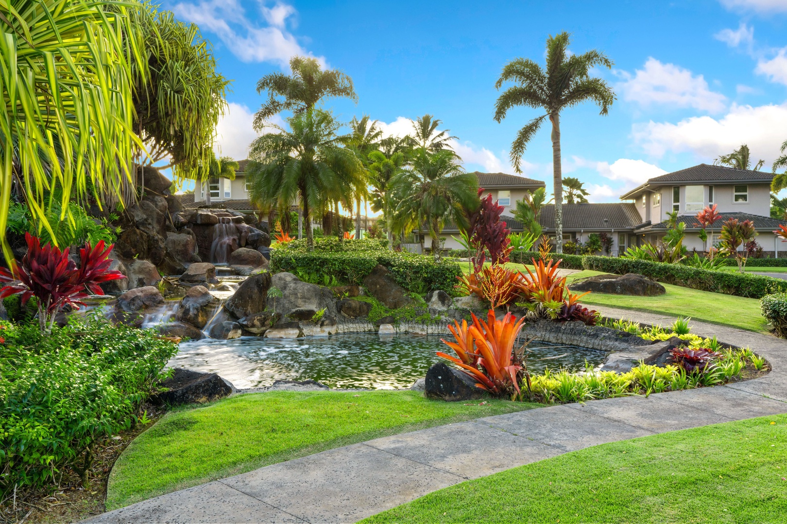 Princeville Vacation Rentals, Noelani Kai - A rock-lined stream curves past red ti plants and palms along the community path.