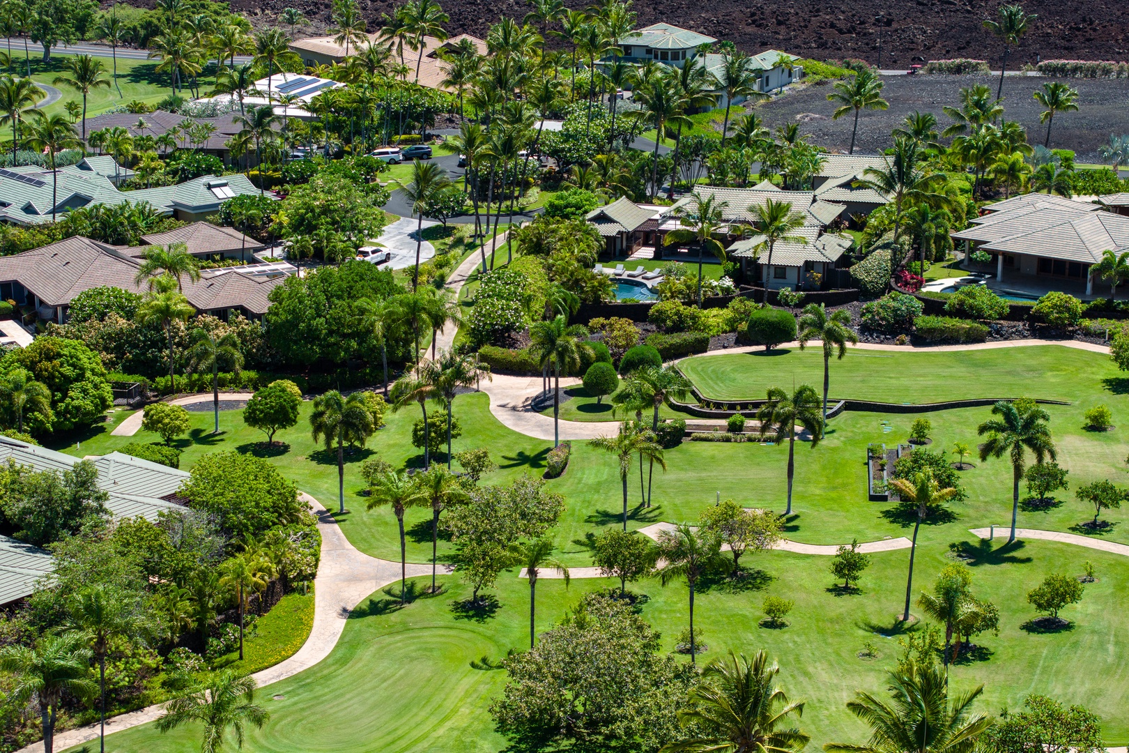 Kamuela Vacation Rentals, Mauna Lani Champion Ridge 22 - A lush, green landscape with winding pathways surrounded by tropical trees and nearby homes.