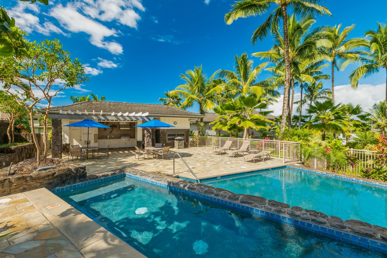 Princeville Vacation Rentals, Kaiulani #8 - Claim a lounge chair on the pool deck, umbrellas up and palms overhead.