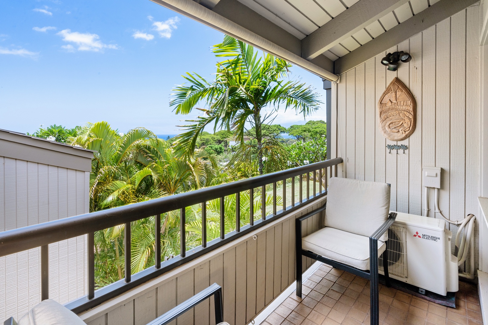 Kihei Vacation Rentals, Wailea Ekolu 204 - Tucked in the corner of the lanai, a single chair catches the palm-framed view, ocean visible in the gap between the trees.