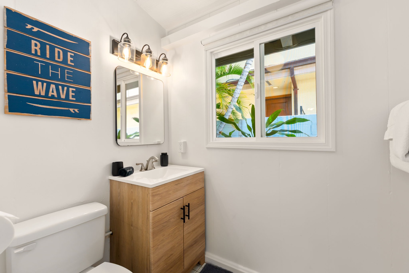 Honolulu Vacation Rentals, Ho'okipa Villa - Step into a bright, coastal-inspired bathroom with warm wood accents, soft lighting, and a window framing glimpses of tropical greenery—your perfect retreat after a day of adventure.